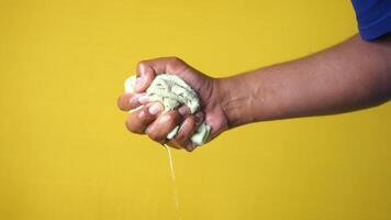 Hands squeeze wet towel against yellow background. draining water from wet towel. video