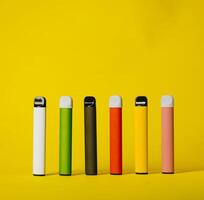 Set of colorful disposable electronic cigarettes with shadows on a yellow background. The concept of modern smoking, vaping and nicotine photo