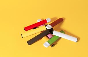 Layout of colorful disposable electronic cigarettes with shadows on a yellow background. The concept of modern smoking, vaping and nicotine. Top view photo