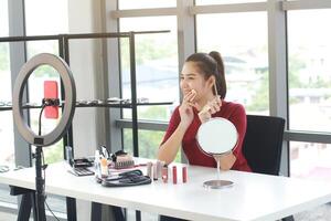 Beautiful Asian woman blogger hand holding Powder puff box and recording on red smartphone for make up tutorial in Cosmetics Vlog website. Youtuber and Marketing in social media concept. photo