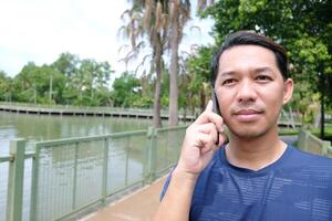Smiling Asain man talking with smartphone in the park. Technology and lifestyle Concept photo