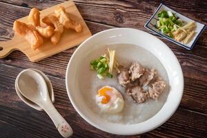 Top view of Chinese rice porridge, Congee with pork, egg and vegetable on wooden background photo