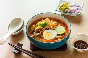 Northern Thai style curried noodle soup with beef and egg on wooden table photo