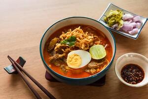 Northern Thai style curried noodle soup with beef and egg on wooden table photo