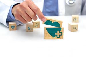 Hand holding a wooden block cube with healthcare medical symbol, heart rate icon and around is a wooden block with blurred icon symbol. Medical and health concept. photo