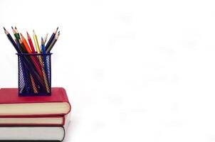 Crayon or colored pencils in box laying on a stack of books, white background. Knowledge and education concept. photo