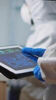 Vertical . Back view of scientist in coverall analyzing virus evolution looking on digital tablet. Team of microbiologists conducting vaccine development using high tech for researching treatment against covid19 video