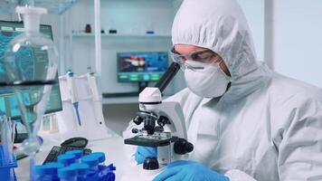 Medical research scientist in coverall conducting vaccine development under digital microscope in a biological applied science laboratory. Lab engineer in ppe suit working on medical treatment video