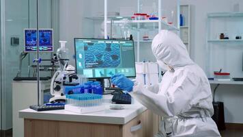 Doctor in coverall taking blood sample tube from rack with machines of analysis in laboratory. Chemists examining vaccine evolution using high tech for research in treatment against covid19 virus video