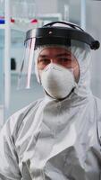 Vertical . Tired doctor in protection suit against covid-19 looking exhausted at camera in equipped lab. Team of scientists examining virus evolution using high tech for scientific research, vaccine development. video