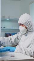 Vertical . Biologist doctor in ppe suit checking liquid sample typing on pc in equipped laboratory. Team examining vaccine evolution in medical lab using high tech and chemistry tools for scientific research video