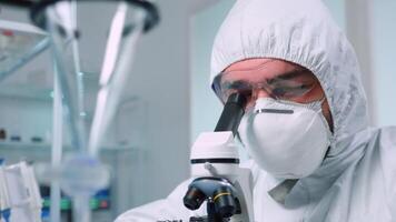 Biochemist in ppe suit looking through a microscope during experiment in sterile lab. Chemist researcher examining virus evolution using high tech for vaccine scientific research against covid19 video