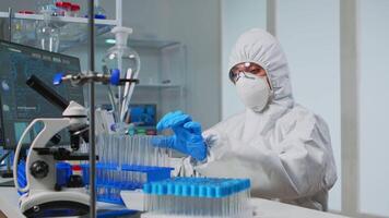 Lab technician in coverall examining samples of liquid typing on computer results sitting in equipped laboratory. Scientist working with various bacteria tissue pharmaceutical research for antibiotics video