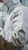 Vertical . Scientist in protection suit looking through a microscope in equipped lab. Team of chemists examining virus evolution using high tech for scientific research of vaccine development against covid19. video