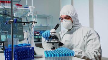 Medical research scientist in ppe suit conducting vaccine development using digital microscope in a biological applied science laboratory. Caucasian lab engineer in coverall working on medical treatment video