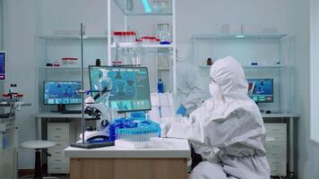 Woman biochemist in coverall checking manifestations of virus working on comuper in equipped lab. Team of doctors examining vaccine evolution using high tech researching diagnosis against covid19 video