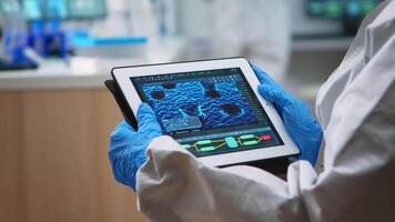 Back view of doctor in protection suit analyzing virus evolution looking on digital tablet. Team of scientists conducting vaccine development using high tech for researching treatment against covid19 video