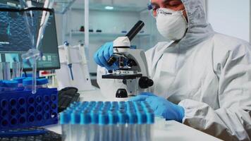 Biological scientist in coverall using microscope doing research for new vaccine in pharmaceutical labolatory. Coworkers examining virus evolution using high tech researching diagnosis against covid19 video