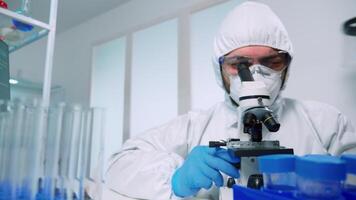 Laboratory scientist in ppe suit conducting experiment looking through a microscope in modern lab. Man working with various bacteria tissue, blood samples, concept of medical research for antibiotics video