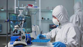 Chemist with coverall analysing bacteria sample from petri dish typing results. Team of doctors examining vaccine evolution with high tech, chemistry tools for research in development of covid19 virus video