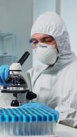 Vertical . Medical research scientist in ppe suit conducting vaccine development using digital microscope in a biological applied science laboratory. Caucasian lab engineer in coverall working on medical treatment video