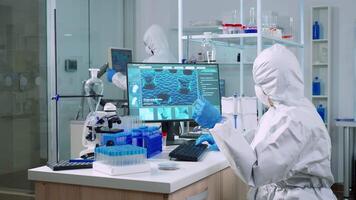 Chemist in coverall checking blood samples taking notes on computer in equipped laboratory. Team of doctors examining vaccine evolution using high tech researching diagnosis against covid19 virus video