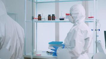 Biochemists nurse in protection suit bringing test tubes in lab room analysing data on computer. Doctors examining virus evolution using high tech for research of treatment development against covid19 video
