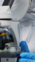 Vertical . Close up of experienced biologist in ppe suit working on microscopes in equipped laboratory. Chemist in coverall examining vaccine evolution using high tech researching diagnosis against covid19 virus video