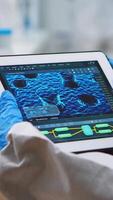 Vertical . Back view of doctor in protection suit analyzing virus evolution looking on digital tablet. Team of scientists conducting vaccine development using high tech for researching treatment against covid19 video