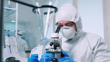 Biotechnology scientist in ppe suit researching DNA in laboratory using microscope. team examining virus evolution using high tech for scientific research of vaccine development against covid19 video