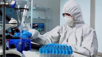 Researcher in coverall testing liquid sample using test tubes for new treatment medical laboratory. Team of doctors examining virus evolution using high tech for vaccine development against covid19 video