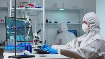 Scientists in protection suits working in chemical equipped laboratory. Team of biologists examining vaccine evolution using high tech and technology researching treatment against covid19 virus video