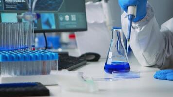 stänga upp av vetenskap tekniker i ppe kostym använder sig av en pipett med en mikrotiter tallrik och en petri maträtt arbetssätt i laboratorium. team granskning virus Evolution för vaccin utveckling mot covid19 video