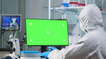 Man researcher in coverall looking at chroma key computer in modern equipped lab. Team of microbiologists doing vaccine research writing on device with green screen, isolated, mockup display. video