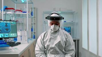 man forskare i ppe kostym ser utmattad på kamera i modern utrustad labb. överarbetad team granskning virus Evolution använder sig av hög tech och kemi verktyg för vetenskaplig forskning, vaccin utveckling video