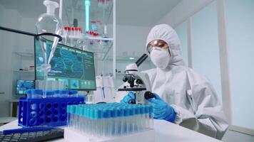 scienziato microbiologia laboratorio nel protettivo completo da uomo conduzione virus analisi guardare attraverso microscopio. squadra di medici l'esame virus Evoluzione utilizzando alto Tech per vaccino sviluppo contro covid19 video