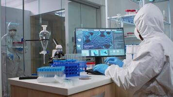 Chemist man in coverall typing on computer analysing vaccine evolution in modern equipped laboratory. Team of doctors in ppe suit using high tech for researching treatment against covid19 virus video