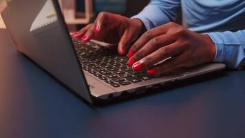 fechar acima do Preto mulher digitando em teclado do computador portátil sentado às escrivaninha dentro vivo quarto ao longo do tempo. africano empreendedor trabalhando atrasado às noite dentro pessoal local de trabalho escrevendo em computador. video