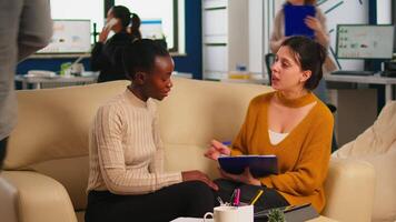 Diverse businesswomen discussing new project for company evolution, black woman checking tasks on clipboard, signing new contract. Multiethnic employees gathered in co-working space video