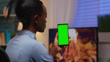 Lady looking at green screen smartphone while relaxing at home sitting on sofa. Woman holding a mobile phone with mockup template chroma key isolated cell phone display using techology internet video