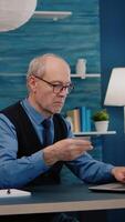 Vertical . Retired man making online payment using credit card on laptop working from home. Senior person shopping online, paying bills, making ecommerce transactions using modern technology via internet video