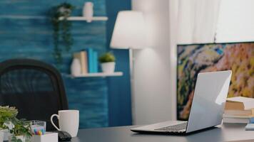 Empty workplace home office with modern design and laptop placed on desk. Living room with nobody in it, place of work, workspace concept, pretty simple modern decor of cozy apartment with television video