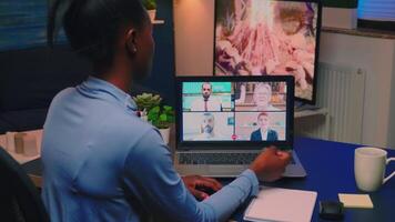 Remote black employee having conference working from home sitting in living room late night. Freelancer using technology network wireless talking on virtual meeting at midnight doing overtime video