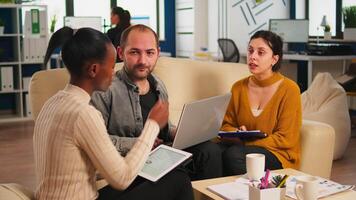 Diverse business people working in teamwork discussing project strategy using laptop sitting on couch at small table. Manager executive analysing financial data from black woman tablet at team meeting video