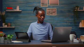 African woman using laptop and tablet in same time in office living room working overtime. Busy focused black employee using modern technology network wireless overworking writing, searching. video