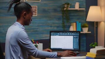 African freelancer analysing digital blue prints checking project of company looking on laptop sitting at desk in living room office late at night overtime. Busy black employee using modern technology video