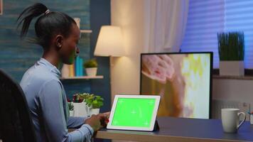 Focused black manager woman looking at tablet with green screen, studying from home using internet technology sitting in living room working overtime. Using mockup chroma key display computer. video