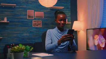 Black businesswoman browsing using smartphone sitting in living room office taking a break after hard work. African remote employee working overtime respecting deadline chatting with team. video