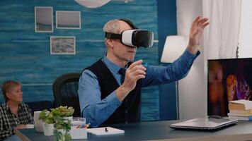 Retired man experiencing virtual reality using vr headset in living room working from home. Old remote employee searching, analysing financial reports while elderly wife watching tv in background video