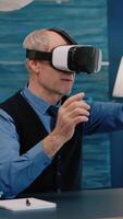 Vertical . Retired man experiencing virtual reality using vr headset in living room working from home. Old remote employee searching, analysing financial reports while elderly wife watching tv in background video